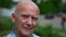 Wise bald old man is looking at camera, portrait of retiree in park at summer, closeup