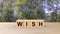 Wish word wooden cubes on table vertical over blur background with forest trees green leaves and sky, mock up, template, to desire