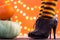 Witch legs in striped stockings and high heel shoes with pumpkins on an orange background, bokeh. Halloween. Copy space.