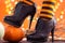 Witch legs in striped stockings and high heel shoes with pumpkins on an orange background, bokeh. Halloween. Copy space