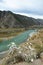 A withered bush with ritual ribbons on a rocky hilltop overlooking the bend of a turquoise river flowing through the valley