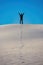 Witness the triumphant spirit of a man raising his hand in triumph with track of footprints at the top of White Sands National