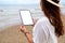 A woamn holding a black tablet pc with blank desktop screen by the sea