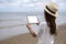 A woamn holding a black tablet pc with blank desktop screen by the sea