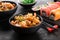 Wok noodles with shrimps and vegetables in a black bowl, sushi roll and seaweed salad on a black textured background