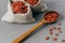 Wolfberries in small cloth sacks and wooden spoon, spread on grey background. Red goji fruit. Whole foods. Healthy diet concept