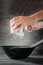 Woma`s hands sift flour over bowl with whisk on dark background