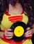 Woman in 1980s yellow clothing holding 45rpm record. Record label painted with yellow poster paint