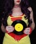 Woman in 1980s yellow clothing holding 45rpm record. Record label painted with yellow poster paint