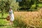 Woman in 40s clothes walks in the Italian countryside, next to a wheat field, carrying a basket of cherries