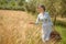 Woman in 40s clothes walks in the Italian countryside, next to a wheat field, carrying a basket of cherries