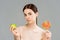 Woman with acne on face holding sweet lollipop and green apple  on grey