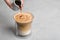 Woman adding caramel syrup to latte macchiato on table