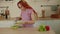 Woman adding fresh cucumber slices in glass bowl with salad in kitchen. Vitamins, dietary and sports nutrition