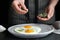 Woman adding herbs to fried eggs at black table