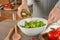 Woman adding olive oil into bowl with fresh vegetable salad on table