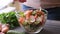 Woman adding salt and spices into mixed salad of vegetables - tomatoes, cucumbers, onion, parsley