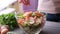 Woman adding salt and spices into mixed salad of vegetables - tomatoes, cucumbers, onion, parsley