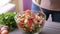 Woman adding salt and spices into mixed salad of vegetables - tomatoes, cucumbers, onion, parsley