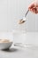 Woman adds psyllium fiber to glass of water on a white background.