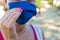 Woman adjusts medical mask with hand with pink manicure. Caucasian girl in blue mask outdoors in hot sunny summer day.