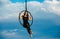 Woman aerialist performs acrobatic elements in hanging aerial hoop against sky
