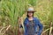 Woman agriculturist standing and catch sugarcane leaf on her right hand, with straw hat and wearing Long sleeve denim shirt in the