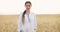 Woman agronomist in white coat standing in wheat field using modern technologies in agriculture