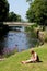 Woman alongside riverbank using mobile phone.