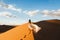 Woman in amazing silk wedding dress, view of Sahara desert sand dunes at sunset