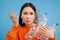 Woman with angry face, holding bottles, recycling plastic waste, complaining, standing over blue background