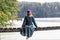 A woman in antique Viking clothes sits on a wooden bridge over a lake.