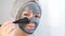 A woman applies a cleansing mask to her face