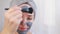 A woman applies a cleansing mask to her face.