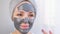 A woman applies a cleansing mask to her face