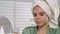 The woman applies the cream to the skin of her face. Portrait of a young woman after a shower in front of a mirror