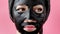 Woman apply black cosmetic fabric facial mask on pink background. Face peeling mask with charcoal, spa beauty treatment