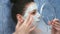 Woman is applying alginate mask in bathr with foam looking at small mirror.