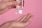 Woman applying antiseptic gel on pink background, closeup