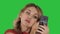 Woman applying black mascara on eyelashes looking in her phone on a Green Screen, Chroma Key.