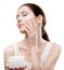 Woman applying emollient cream from container on face