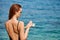 Woman applying sunscreen creme on tanned shoulder over the sea