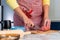 A woman in apron cooks in the kitchen, cuts sausage. Hands close-up. The concept of homemade food
