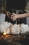 Woman in apron sprinkling sugar powder on christmas gingerbread houses on rustic wooden table. Atmospheric moody image. Christmas