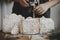 Woman in apron sprinkling sugar powder on christmas gingerbread houses on rustic wooden table. Atmospheric moody image. Christmas