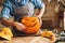 Woman in apron standing in kitchen and carving large orange Halloween pumpkin