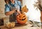 Woman in apron standing in kitchen and removing all the pulp from Halloween pumpkin