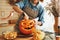 Woman in apron standing in kitchen and removing all the pulp from Halloween pumpkin