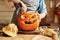 Woman in apron standing in kitchen and removing all the pulp from Halloween pumpkin