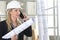 Woman architect or construction engineer talk on the mobile phone wear helmet and holds blueprint inside a building site with